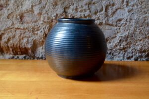 Ce joli vase boule est le fruit de la poterie Echinger. Sa forme géométrique et sobre est mise en lumière par les fameux émaux noir à l'aspect à la fois brillants et mats caractéristiques. La forme sphérique du vase est finement mise en valeur par les décors annelés. La pièce est signée en creux sur le dessous.