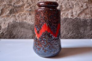 Production ouest-allemande vintage, ce vase cylindre ou rouleau est typique des productions Fat Lava. Doté d'un émaillage riche, brillant à l'aspect cristallisée et d'un joli trait rouge vif et dynamique; c'est une jolie pièce décorative à la présence affirmée.
