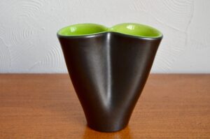 Ce vase Elchinger s’inscrit parfaitement dans les recherches formelles des créateurs midcentury. Les formes se libèrent, se détachent de tout académisme ou des références historiques. Ce joli vase mouchoir est doté d'une forme tout en souplesse et arrondis, libre et sculpturale. Le traitement bicolore, l'émaillage mat/brillant, sur les faces interne et externe du vase renforce l'idée de volute et de forme dynamiques, transformant un objet commun en sculpture abstraite!