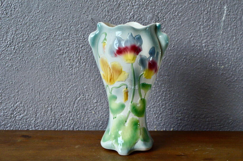 Réalisé selon des modèles de la fin du XIXe siècle, ce grand vase au fleur est une production des ateliers lorrains de Saint Clément. De belles taille, de forme élancée et travaillée il est réalisé en barbotine colorée et largement fleurie. Pièce de décoration bohème, décoration typiquement française, elle apportera sa touche printanière et classique à un intérieur contemporain. 