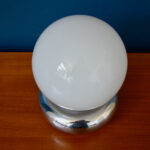 Comme une lune posée sur un anneau de métal, cette jolie lampe est une production italienne des années 70. Une large sphere de verre opalescent est disposée sur une pièce de métal chromé. L'ensemble est très graphique, sobre élégant et diffuse une douce lumière dans toutes les directions. Parfaite lampe d'ambiance, elle se mettra en valeur et apportera sa touche spatiale à la déco intérieure.