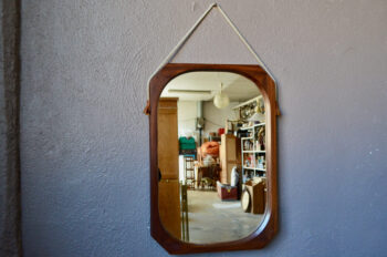 Ce magnifique miroir italien est doté d'un épais cadre en teck massif. Le bois est élégamment facetté, travaillé dans l'épaisseur de la matière. Il est suspendu par une cordelette, dont les extrémités sont habillées par des pièces de cuir. C'est une pièce rare, de très belle facture. Dans une entrée ou une salle d'eau, ce miroir des années 60 sera une belle pièce de déco murale, sorte de bulle de lumière.
