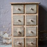 Sublime meuble à tiroirs, cette commode à la patine divine provient d'un ancien atelier. Ses lignes sobres fonctionnelles sont touchantes et emplies de détails émouvants : les boutons en bois tourné sont lustrés par les années, les tiroirs sont hauts et nombreux. La patine est authentique, prononcée, le bois est grisé par des anciennes couches de peinture anciennes, le meuble d'atelier est en chêne et sapin. Le meuble se présente dans un format de commode haute et étroite, type chiffonnier, il se glissera dans tous les espaces.