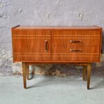 Cette jolie petite enfilade des années 60 est à la fois simple et originale. Son caisson est joliment souligné par des lignes horizontales. Il comprend plusieurs espaces de rangement : un caisson et deux larges tiroirs. Ces dimensions pratiques en font un meuble TV ou Hifi idéal. Des boutons originaux en métal noir doré complètent le look rétro et pétillant de ce meuble sideboard qu'on imagine dans l'entrée ou le salon.