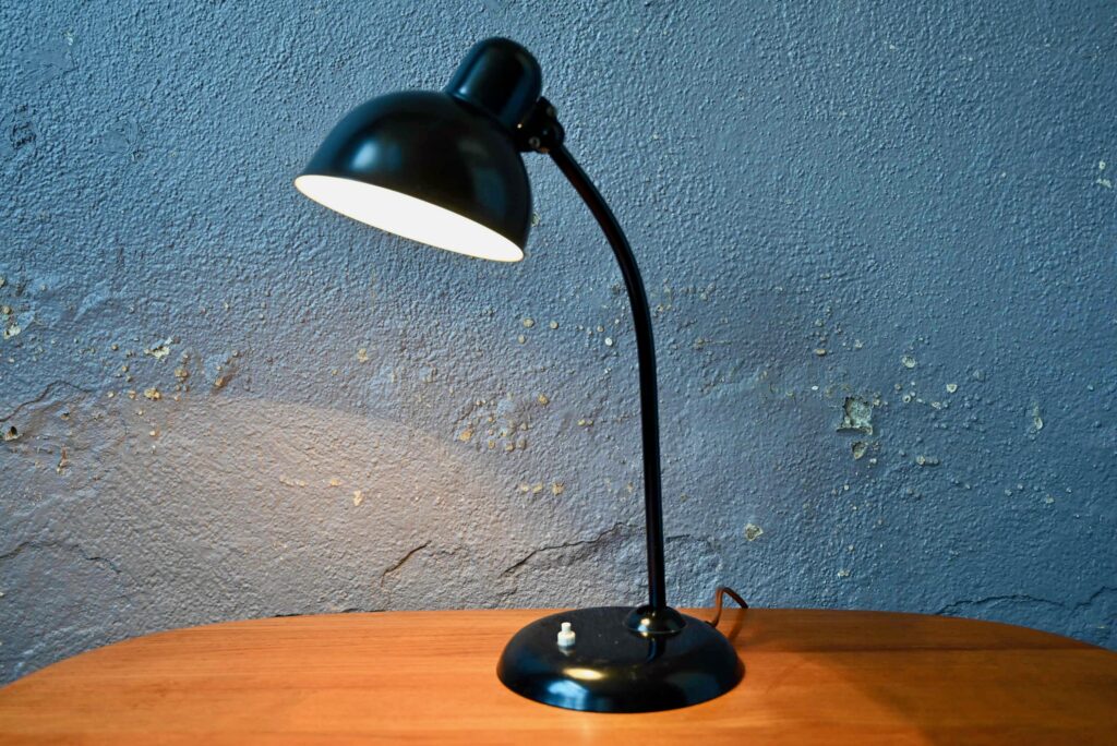 Dessinée par Christian Dell et fabriquée et distribuée dans les années 30 par l'entreprise Kaiser Dell, la lampe 6551 est une icône du design de l'entre deux-guerre. Cette lampe de bureau est tout à fait dans les codes de production des années Bauhaus. Son design à l'allure sobre et élégante est basé sur la fonction d'éclairage, un esthétisme simple et efficace, et une facilité de production en série. Elle est réalisée en métal avec des pièces moulées et un minimum de soudures. Cet exemplaire de la lampe 6551 est une édition originale dans dans un état de conservation exceptionnel.