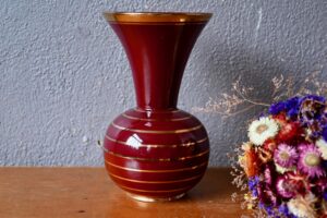 Ce joli vase au col ouvert le fruit de la poterie Elchinger. Ses formes généreuses sont mises en lumière par l'association d'un rouge vif et du doré. La pièce est signée en creux sur le dessous. Pièce démonstrative, elle saura mettre en valeur un meuble midcentury ou un beau bouquet !