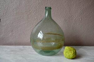 Destinée jadis à la conservation des liquides, les anciennes dames Jeanne fleurissent aujourd'hui dans nos intérieurs. Celle-ci est de petite taille et d'un joli vert bouteille. Elle est ancienne et sera parfaite dans un cocon aux accents campagne chic.